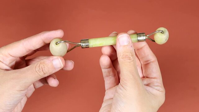 hands holding a green jade facial roller isolated on orange background