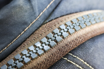 Detailed macro shot of grey zipper on blue fabric, clothing fastener showing sturdy texture of textile, strong seam and an industrial fashion design detail © CoreRock