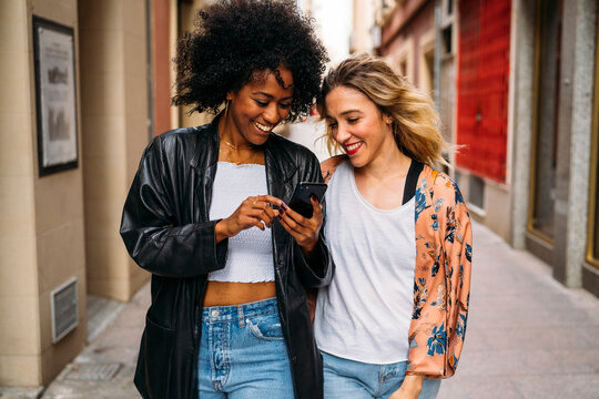 Diverse friends enjoying smartphone walking urban street
