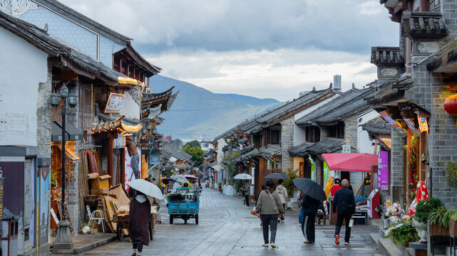 People with umbrellas walking through an ancient town street with traditional Chinese architecture on a rainy day.