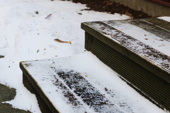 Close-up of wooden steps partially covered with snow, showing winter weather, cold conditions, and outdoor architecture in a quiet natural setting.
