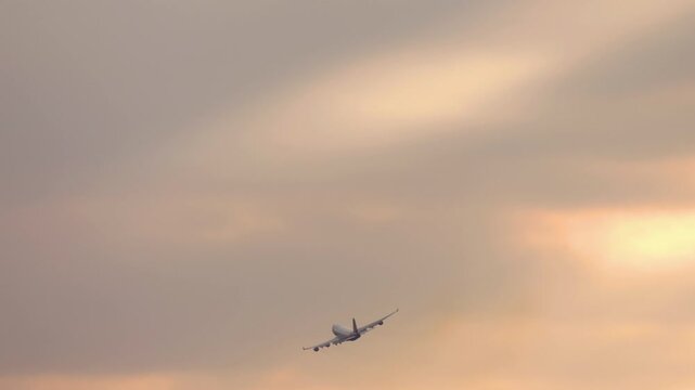 Wide-body four-engine aircraft ascending into the colorful sky during sunrise or sunset. Symbol of air travel and long-haul aviation.