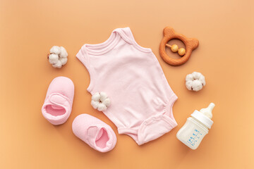 Pink baby bodysuit with wooden teethers and bottle of milk on pastel beige background, top view
