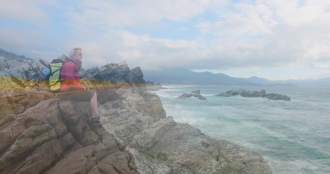 Mature male hiker sitting on rocky cliff gazing at ocean, with animated marketing charts