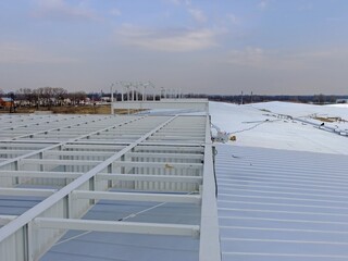 Metal roof construction in progress features structural steel supports against a cloudy sky.