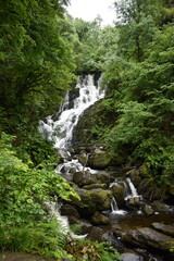 Obraz premium A waterfall cascades down moss-covered rocks surrounded by trees and green vegetation