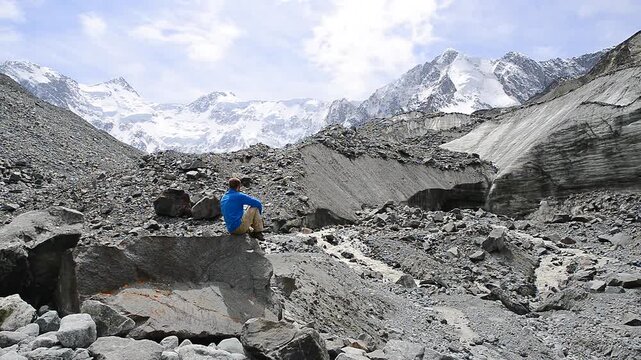 A guy sits on a rock at the foot of the Akkem glacier in Altai and admires its grandeur.