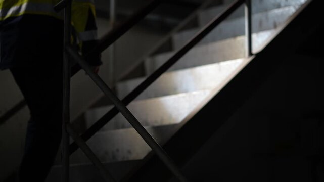 Worker's silhouette on dimly lit staircase with metal handrail in industrial indoor setting