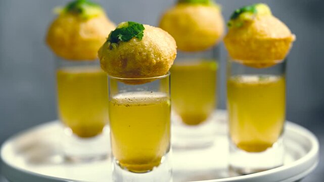 Close up of Indian street food fuchka on a glass with sour spicy water.  Pani puri a chat item in India. 4K indian street food snacks.