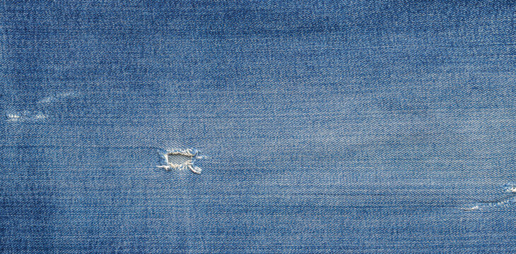 Blue denim fabric with worn texture and small rip