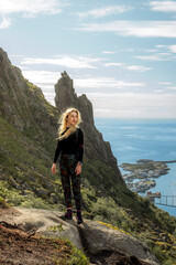 Obraz premium White blonde woman standing on a hike in Lofoten with city in the background