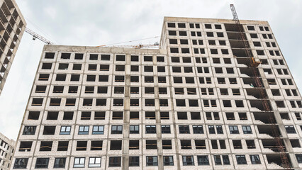 Fototapeta premium Unfinished high-rise apartment building under construction with visible concrete structure and cranes above, symbolizing architecture, engineering, and urban development concepts