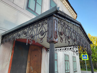 On a summer day, an old rusty wrought-iron canopy over the entrance to a building.