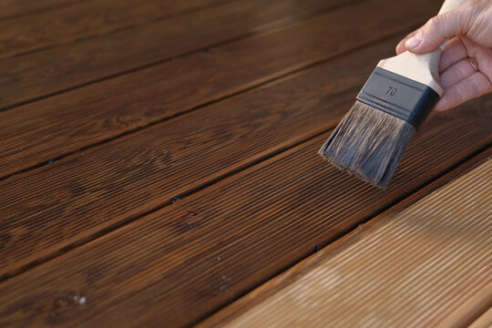 Brown oil for protection of wood by staining. Painting a larch for protecting and pests. Woodworker applying finish to terrace deck board. Repairman varnishing with brush wooden plank floor surface.
