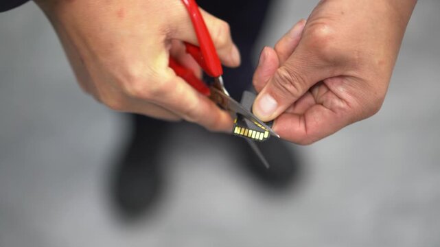 Close-up of hands using red-handled scissors to trim a metal component