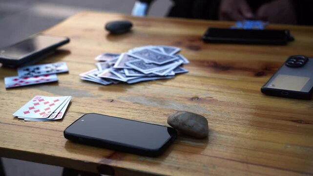 Wooden table surface with scattered playing cards and multiple smartphones