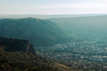 Obraz premium Wide landscape view overlooking Mostar and the Neretva valley, showing mountains, urban area and natural terrain in calm atmospheric conditions.