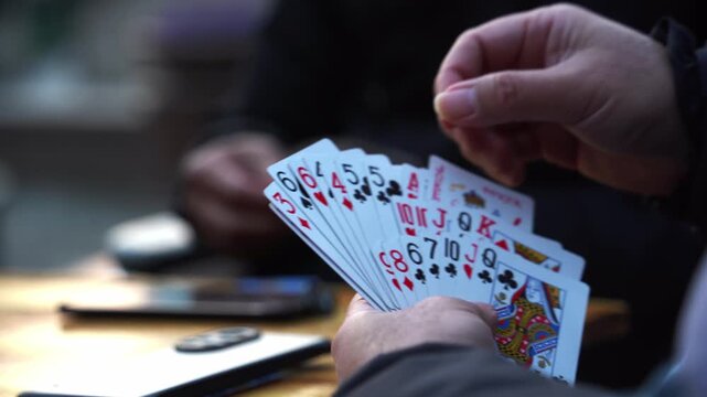 Close-up of a hand holding five playing cards showing suits and numbers