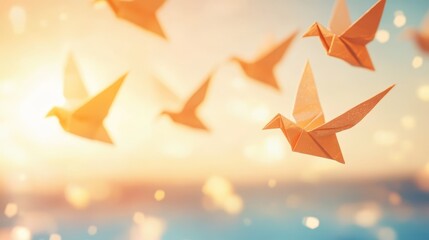 Many orange origami doves appear to be flying towards a bright, warm sunset or sunrise sky with a soft bokeh background