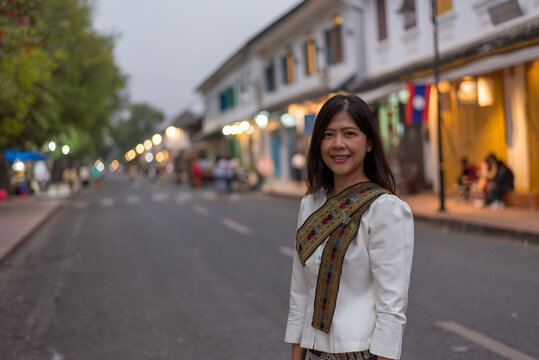 A smiling woman in traditional Lao attire on a charming street in Luang Prabang during morning. Beautiful daylight portrait at a famous UNESCO World Heritage site in Laos.