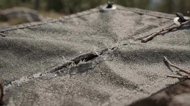 Medium shot of a durable tarp fabric with selfhealing microcapsule coating visibly repairing small tears under light stress outdoors.