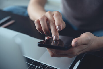 Close-up iof casual business woman using smartphone while working on laptop computer at home...