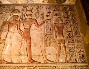 Egyptian wall art shows three figures adorned with headdresses, depicted in relief against stone carvings and hieroglyphs