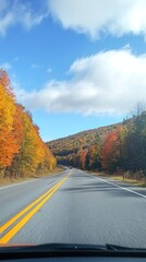 Scenic Autumn Drive Through Vibrant Forested Hills Under a Cloudy Blue Sky