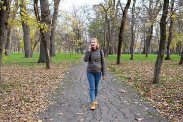 Obraz premium Woman walking on park path while talking on mobile phone during autumn season. Concept of wireless communication