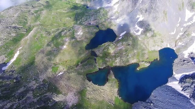 Aerial view of alpine lake surrounded by tundra meadows in the Rocky Mountains at high altitude. Clear summer light reveals rugged peaks and pristine wilderness across remote American ranges.