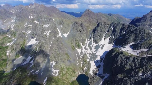 Aerial view of alpine lake surrounded by tundra meadows in the Rocky Mountains at high altitude. Clear summer light reveals rugged peaks and pristine wilderness across remote American ranges.
