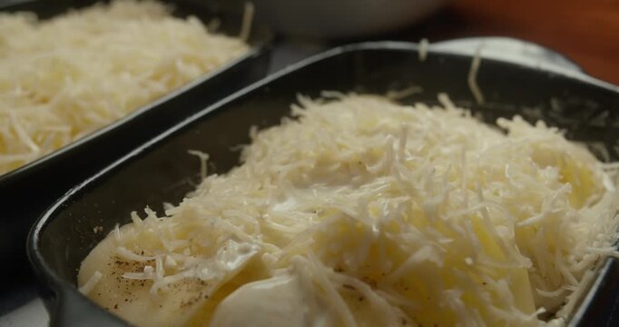 Chef pours creamy white b chamel sauce over layered sliced potatoes and cheese in cast iron baking dishes. Close-up of cooking process, homemade comfort food, classic French sauce,