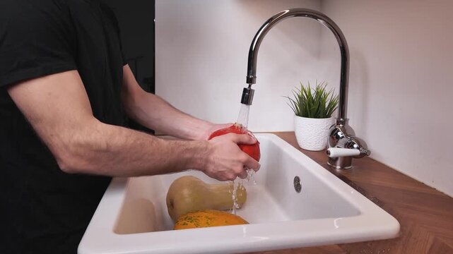 Man washing an orange red kuri pumpkin in kitchen sink, top view