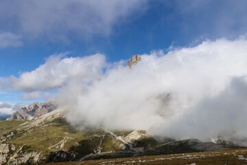 Hiking trail perspective of Tre Cime di Lavaredo massif under dramatic white clouds