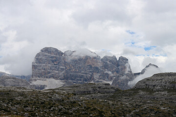 Cloud‑veiled Tre Cime di Lavaredo rising above alpine trails in northern Italy
