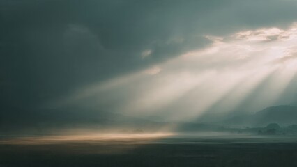 Naklejka premium Dramatic landscape with sun rays breaking through clouds over misty mountains