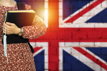 Student Woman Holding Books in Front of British Flag Backdrop with Mask in Hand