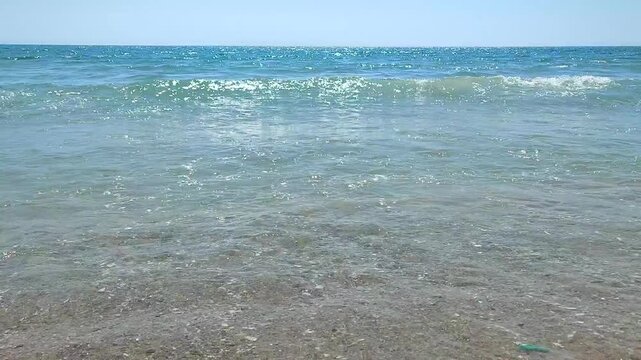 Sea waves with turquoise transparent water rolling onto sand of sandy beach on sunny summer day. Quiet, calm, windless sea. Low angle. From below. Nobody. Nature backdrop. Natural background