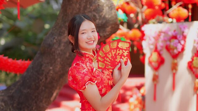 During the Chinese New Year celebration, a young woman in a traditional red qipao (cheongsam) holds a red envelope.