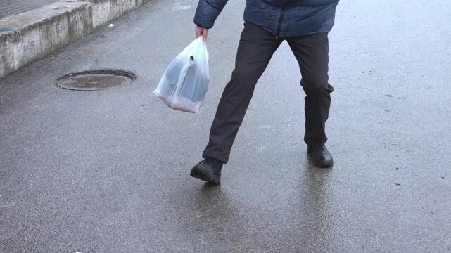Man with a plastic bag slips on an icy road, barely keeping his balance
