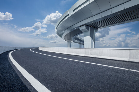 An empty asphalt road and a modern overpass under a clear blue sky on a sunny day