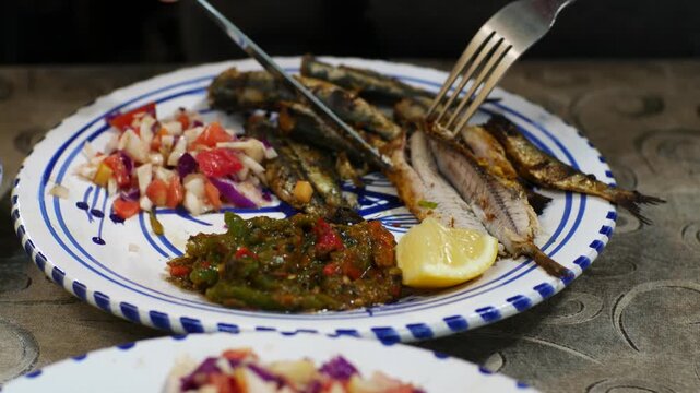 Traditional Tunisian meal, grilled sardines served with mechouia salad and lemon on a ceramic plate. Authentic North African cuisine, rustic food presentation, close-up view selective focus