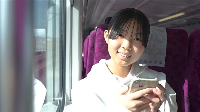 電車でスマホを見る10代の女性