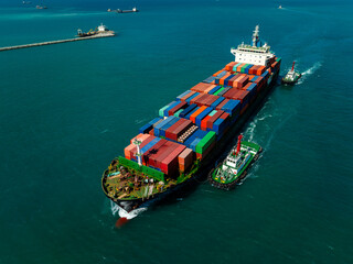 Aerial view of container ship leaving industrial port with tugboats passing breakwater
