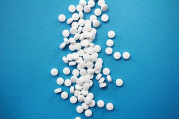 A large scatter of round white pills lies on a vibrant blue background, symbolizing health, medicine, and pharmaceutical healthcare concepts