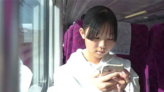 電車でスマホを見る10代の女性