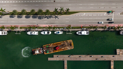 Ocean water canal with empty floating docks next to road with palm trees with moving traffic on side
