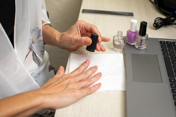 Woman working and doing manicure on work desk with laptop computer next to hands