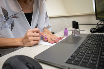 Woman working and doing manicure on work desk with laptop computer next to hands