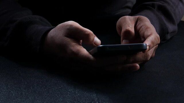 Phone scammers, unrecognizable man holding a smartphone, anonymous cyber criminal performing phishing attack, identity theft via mobile phone, threat to privacy and digital security.